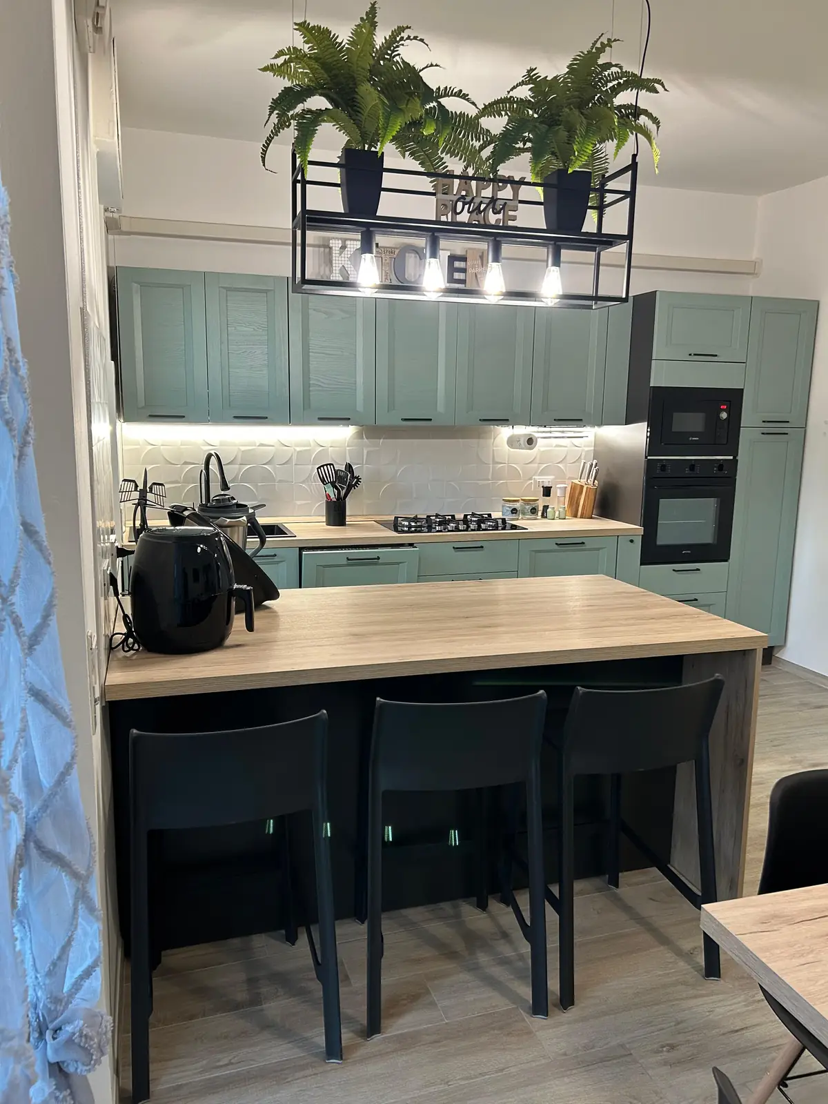 Cucina verde con isola in legno e sgabelli neri