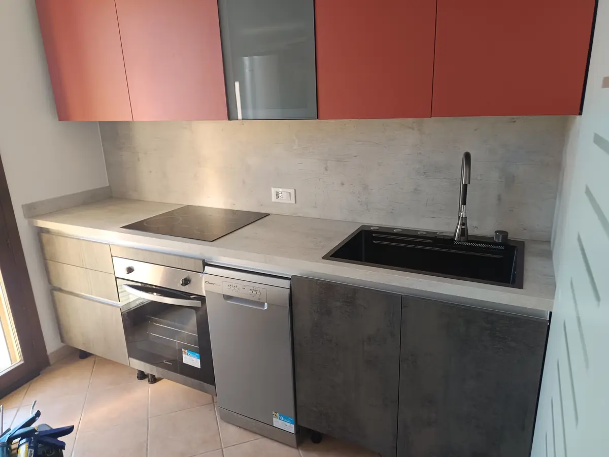 Cucina moderna con pensili rossi, basi effetto cemento e lavello nero