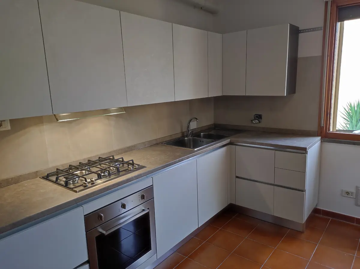 Cucina su misura moderna ad angolo con ante grigio chiaro, piano effetto pietra e forno a incasso